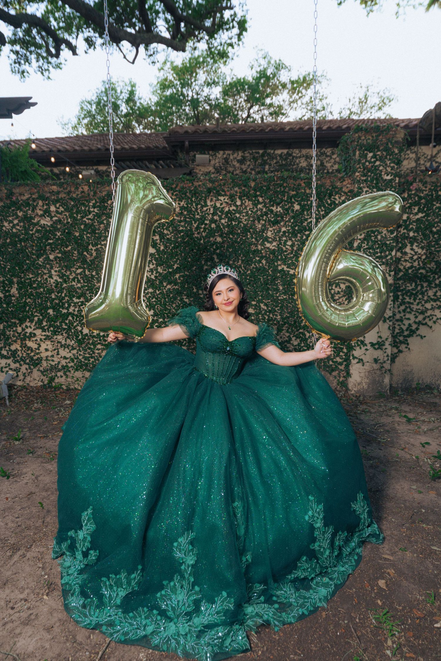Emerald green ball gown with metallic number balloons in garden setting.