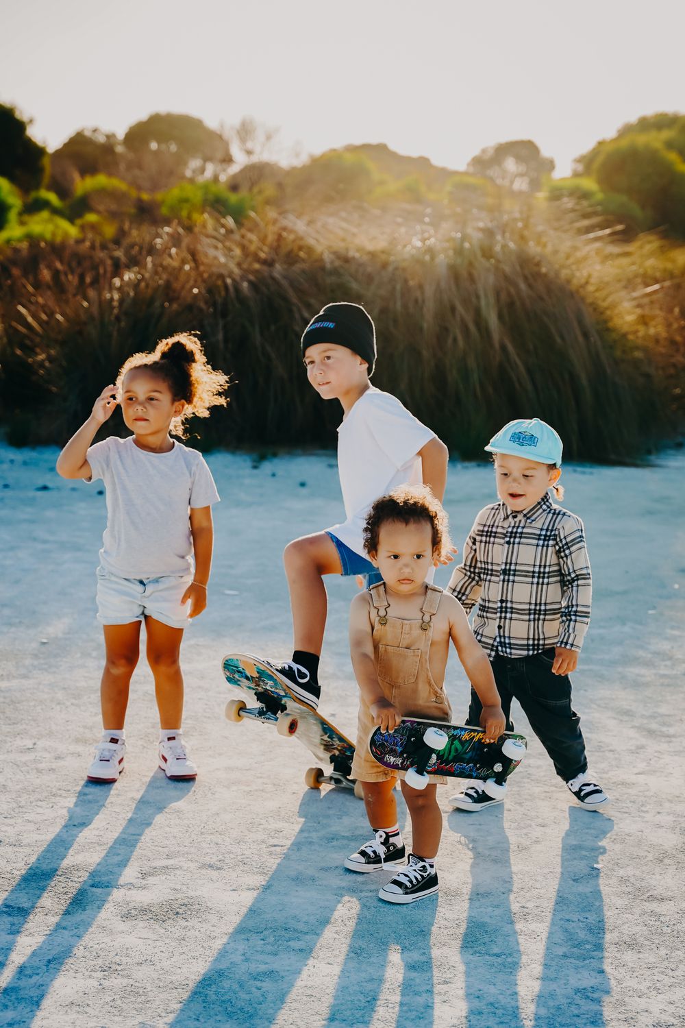 A group wearing casual clothes and sneakers poses together outdoors on a sunny day with a skateboard.