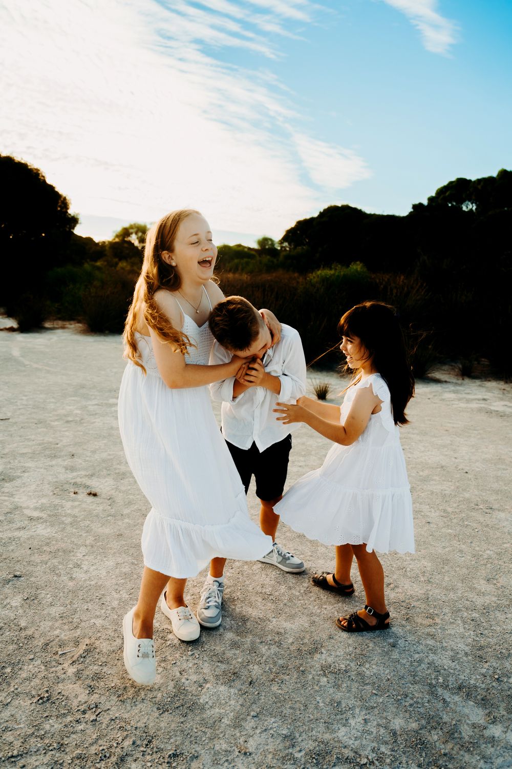 A joyful family moment captured in white dresses playing together on a sandy beach during golden hour.