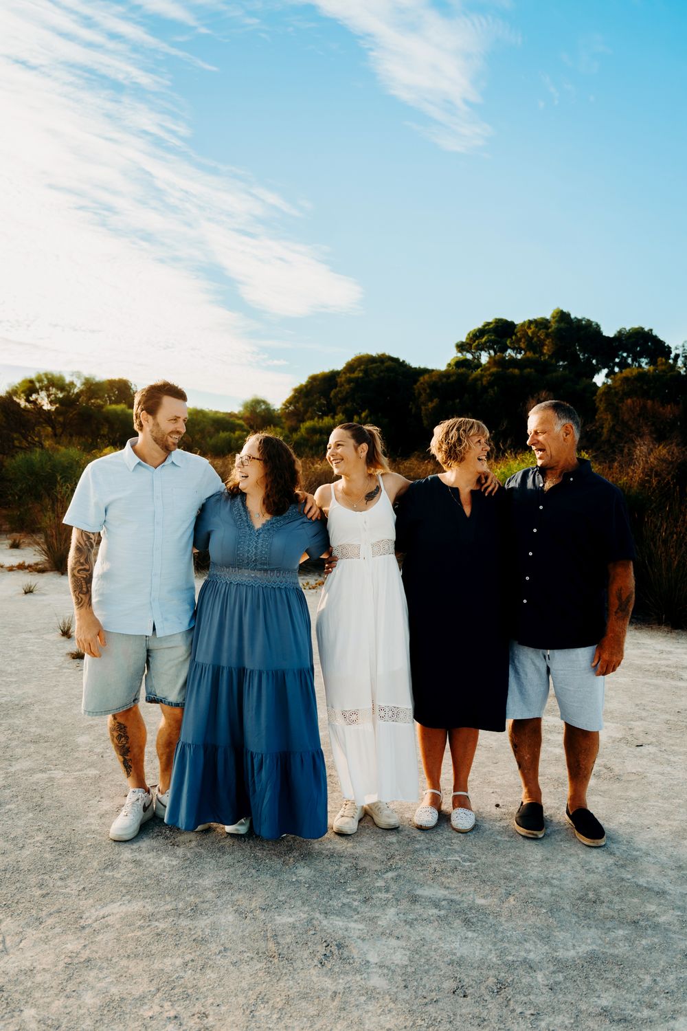 Group of people wearing coordinating blue and white outfits pose along a sandy beach at sunset.