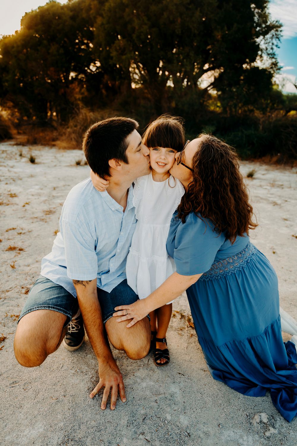 An intimate family portrait shows a tender moment of affection on a sandy beach at sunset.