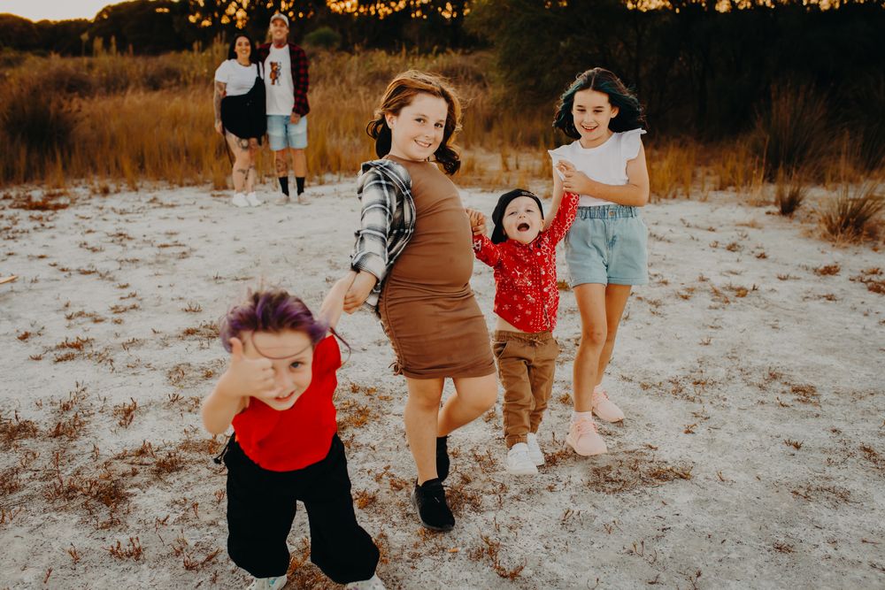 A group of people playing and running together on a sandy beach at sunset.