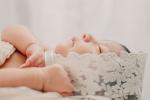 Sleeping newborn baby wrapped in delicate lace on white bedding.