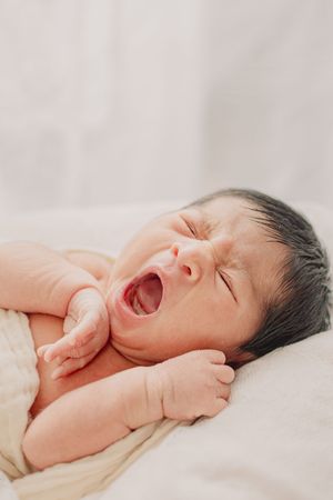 Newborn baby yawning while resting on soft white bedding.