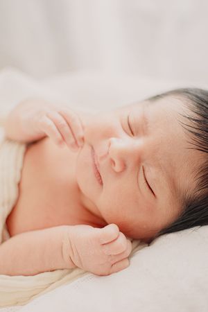 Serene portrait of sleeping newborn on white bedding with gentle lighting.