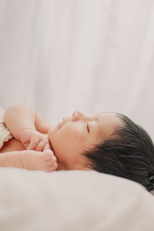 Peaceful sleeping newborn baby lying on white bedding in soft lighting.