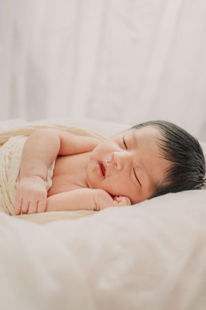 Newborn baby sleeping peacefully on cream-colored bedding with natural lighting.