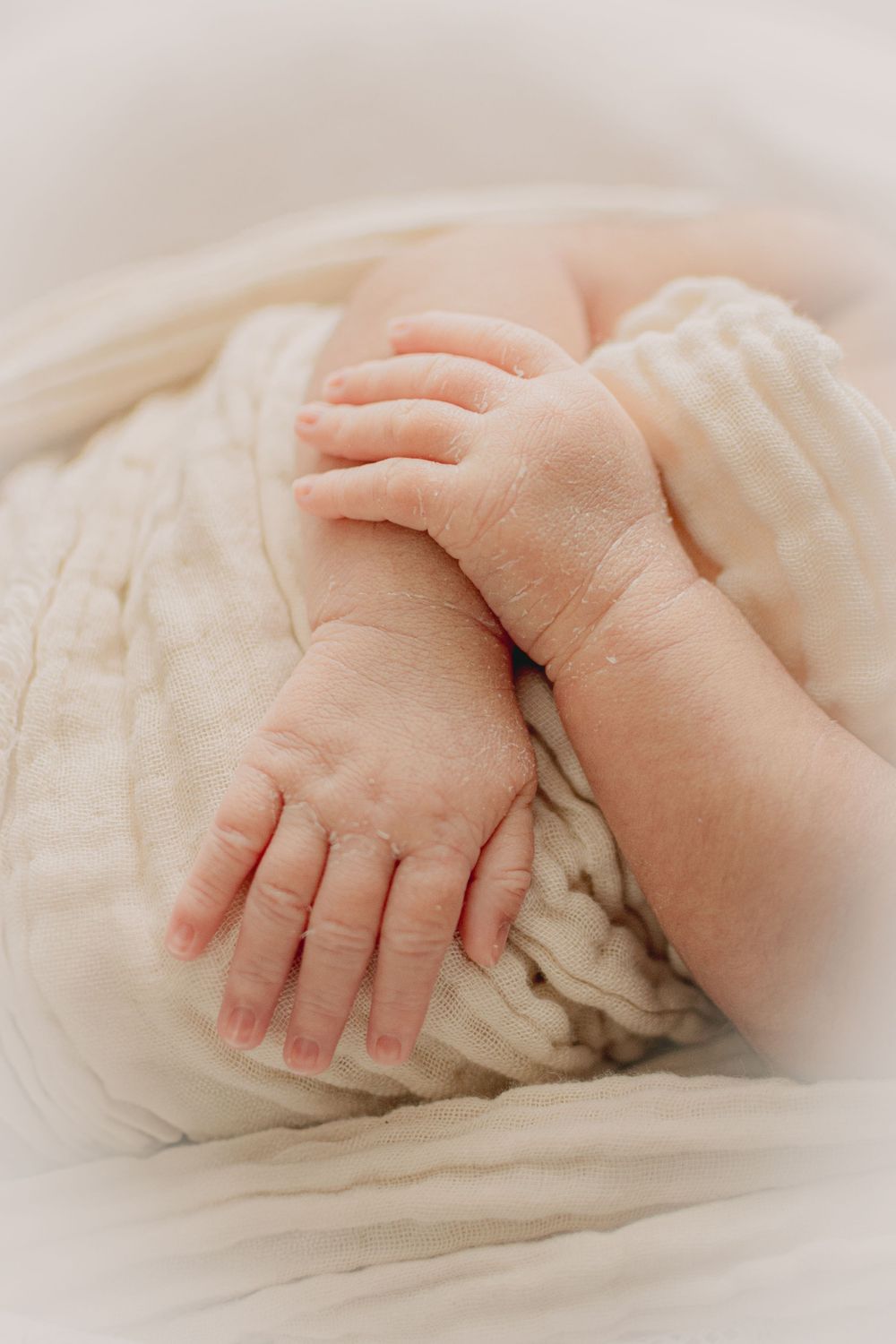Close-up of tiny baby hands resting on soft white knitted fabric.