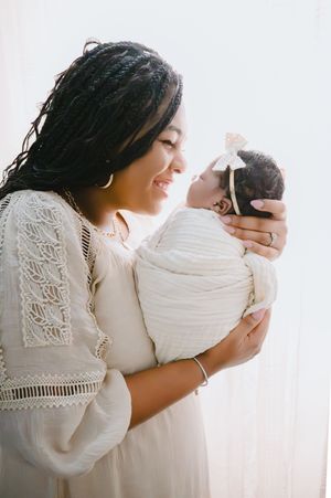 A tender moment captured in soft light showing a parent holding and embracing a newborn baby in white clothing.