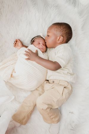 Sweet moment between siblings as they cuddle on plush white background.