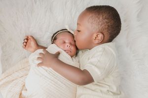 Tender moment between siblings sharing affection while resting on white furry surface.