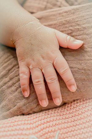 Close up of small child's hand resting on textured brown fabric.