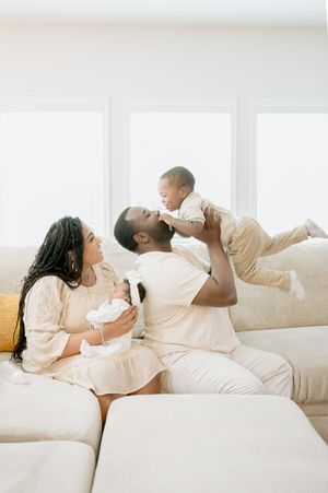 Family sharing joyful moment together on white couch in coordinated cream outfits.