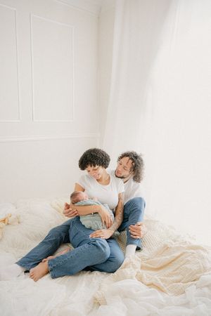 A couple relaxes together on white bedding in a bright, minimalist room.