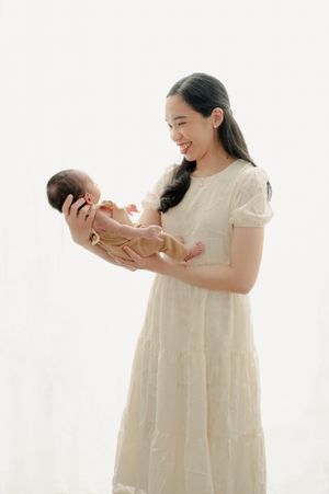 Woman in cream dress holding newborn baby against white background in studio setting.