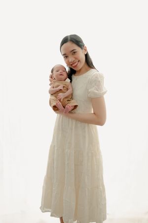 Mother in white lace dress sharing tender moments with newborn baby in bright studio setting.