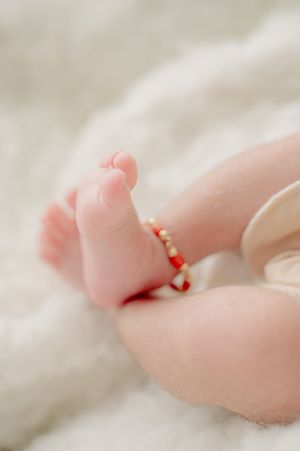 Close-up of tiny baby toes with red string anklet against white background.