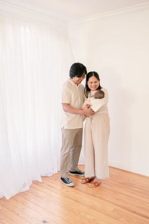 Family of three standing together near white curtains in minimalist room.