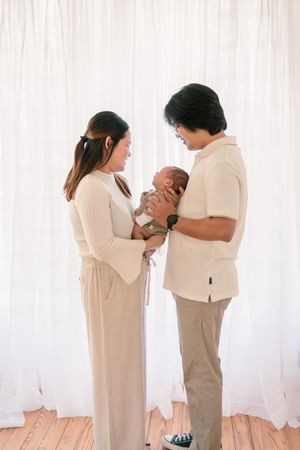 Parents in matching beige outfits gazing lovingly at their newborn baby.