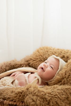 Baby lying on soft brown textured blanket in studio setting with white background.