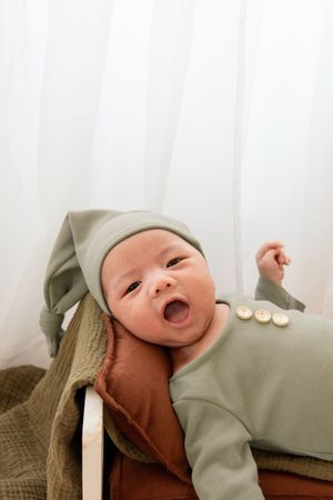 Smiling baby in sage green outfit with white hat during photo session.