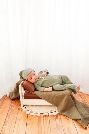 Baby in sage green outfit lying on wooden floor during lifestyle photoshoot.
