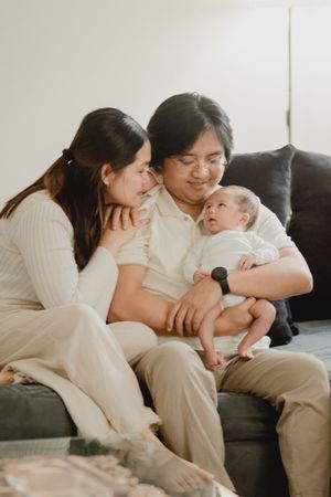 A tender family moment on a gray couch as they cuddle with their newborn baby in matching cream sweaters.