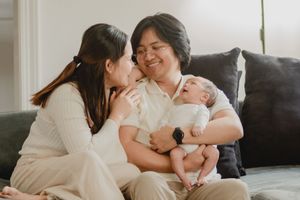 Intimate family bonding moment with a baby on a dark couch in soft natural lighting.