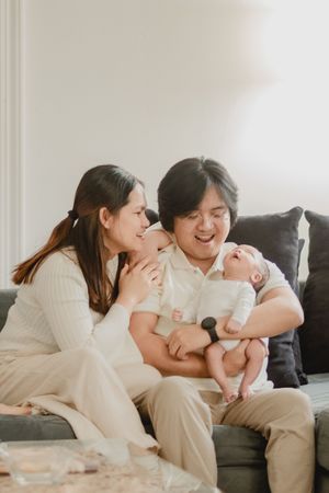 Sweet candid moments of a family sharing laughs and cuddles with their infant on a gray sofa.