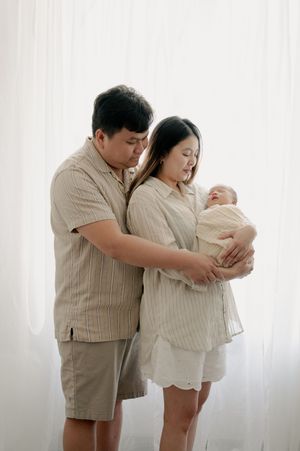 Couple in casual beige clothing embracing while holding their newborn.