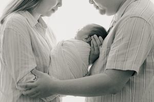 Black and white portrait of parents tenderly holding newborn baby.