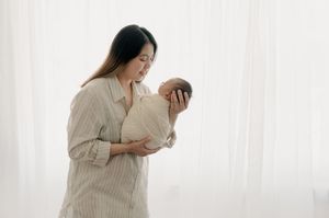 Side profile of mother holding newborn baby near bright window.