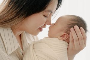 Intimate close-up of mother cradling sleeping newborn in natural light.