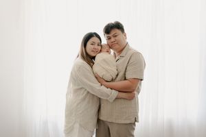 A couple wearing neutral colored outfits embrace lovingly against a white background.