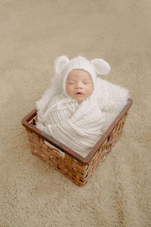 Newborn baby wearing white bear hat sleeping peacefully in woven basket.