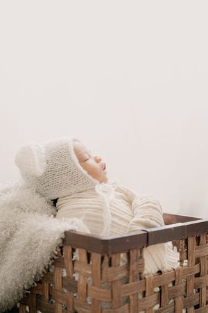 Baby wearing knit hat sleeping in woven basket with textured blanket.