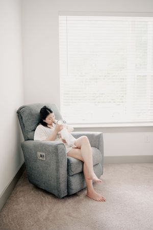 Person relaxing in grey recliner chair next to window.