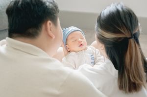 A newborn baby wrapped in a white blanket lies peacefully on a soft surface.