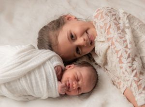 Two young children rest together on white bedding wearing matching outfits.