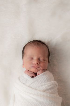 A peaceful newborn swaddled in white fabric sleeps soundly.