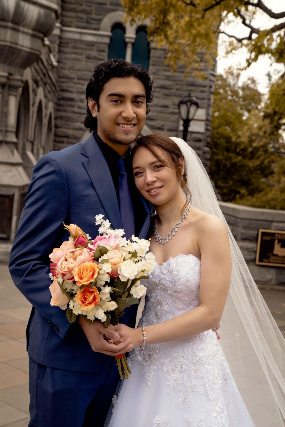 A wedding portrait showcasing a beautiful couple in autumn with stone architecture in the background.