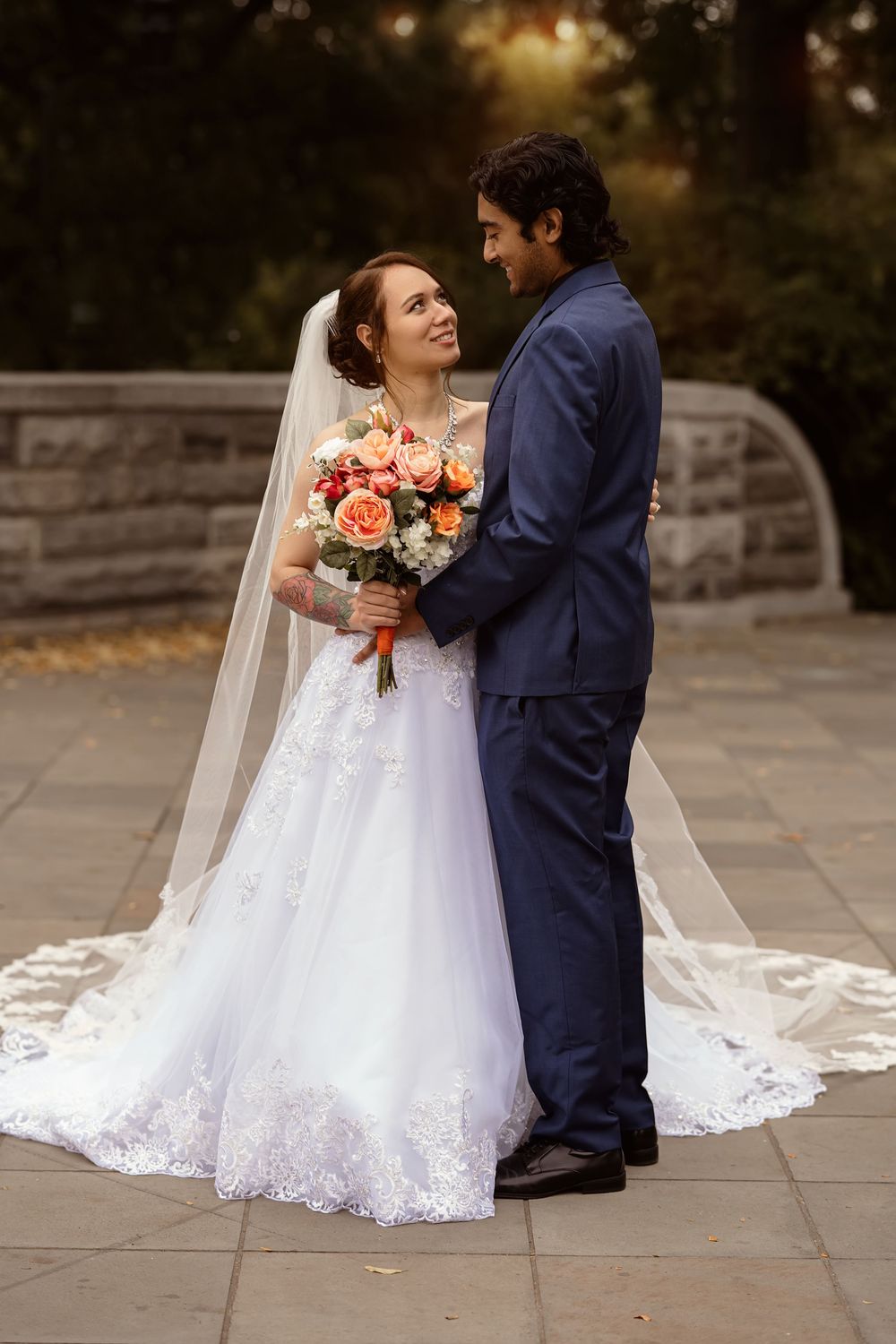 A joyful wedding couple shares a tender moment on a stone pathway with a flowing white dress.
