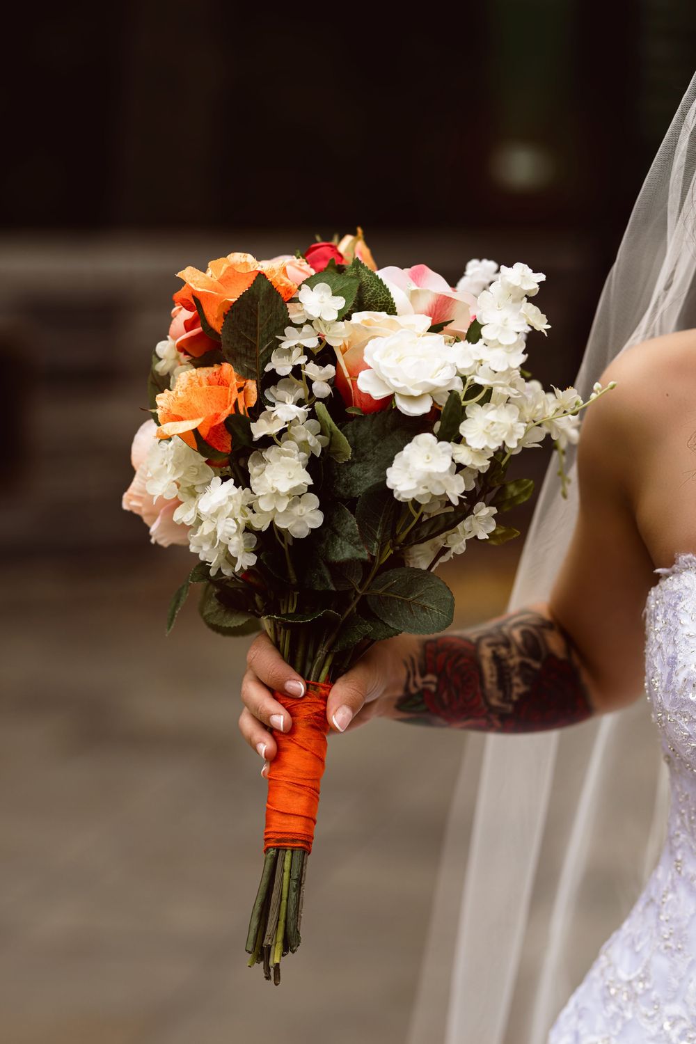 A bridal bouquet featuring coral roses and white flowers wrapped with orange ribbon.