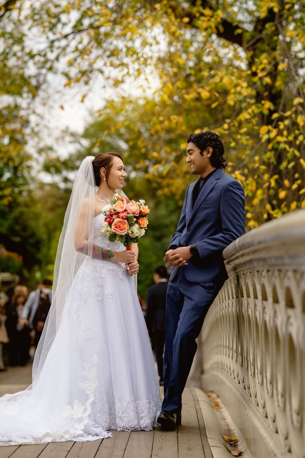 A romantic wedding couple poses on a bridge with autumn foliage and stone architecture.