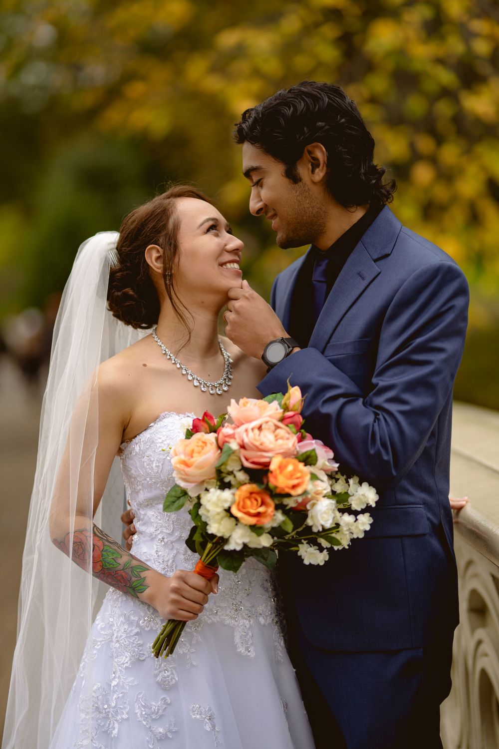 An intimate wedding portrait with autumn foliage and coral roses in the bouquet.