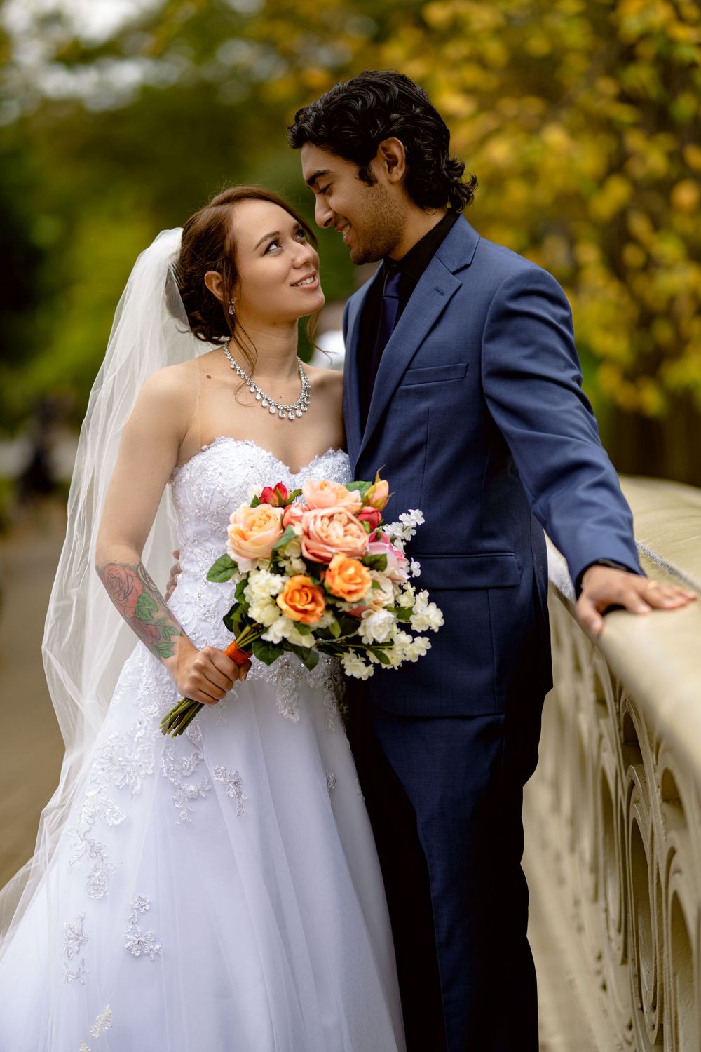 Romantic autumn wedding portrait featuring a couple in white dress and navy suit with peach and white bouquet on bridge.