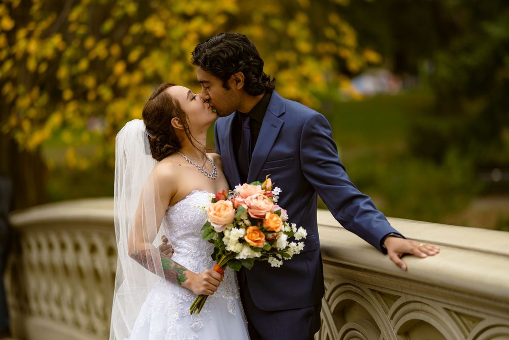 Romantic wedding moment captured on bridge with fall foliage and peach floral bouquet.
