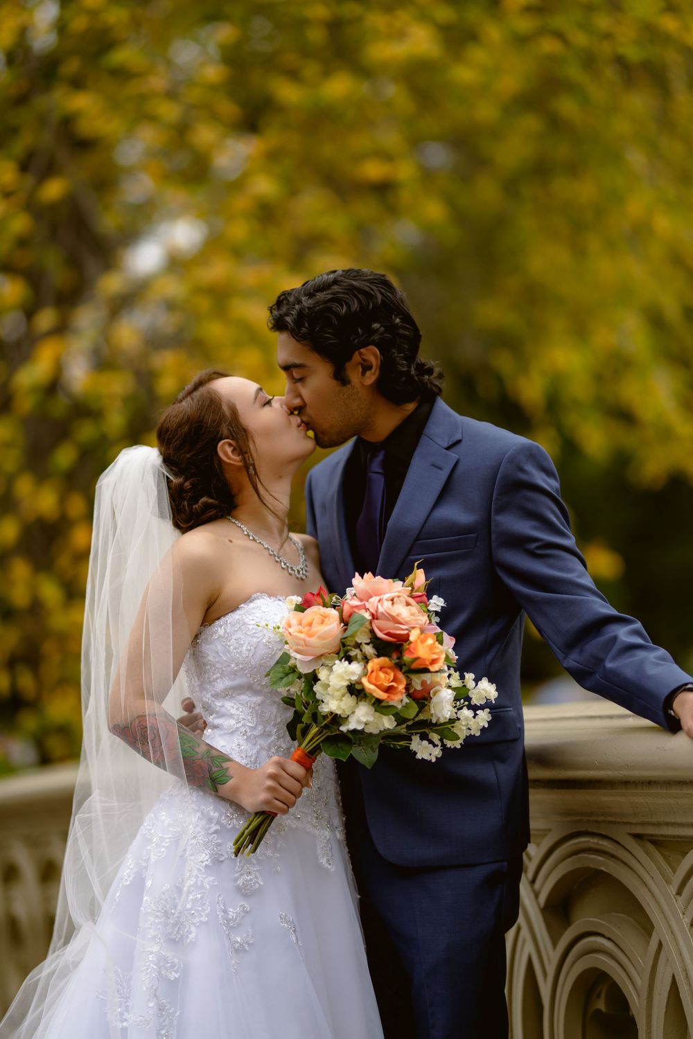 Intimate wedding portrait with couple embracing on decorative bridge surrounded by fall colors.