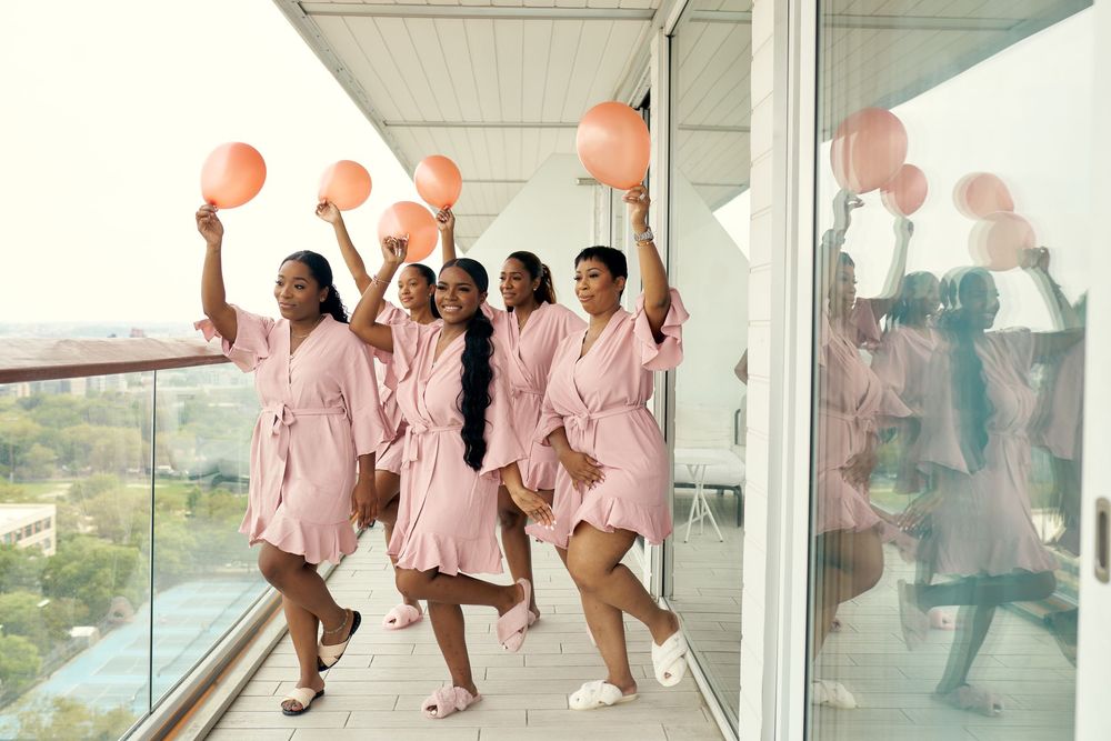 Bridesmaids in pink robes celebrate with balloons on a high-rise balcony. at the WIlliam Vale Hotel