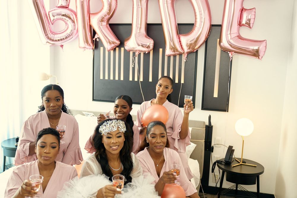 Bridal party in pink robes celebrates under rose gold BRIDE balloons during pre-wedding festivities. at the WIlliam Vale Hotel